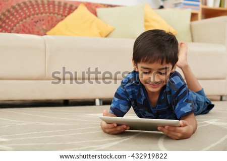Smiling boy lying on floor and watching movie on tablet
