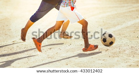 An action picture of the kids are playing soccer football in the sunshine day. Focus on the legs and ball.