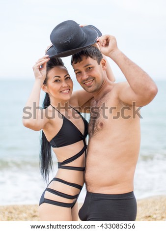 Couple on seashore in cloudy day. Attractive young couple in black swimwear posing with one for two hat