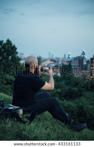 portrait of long bearded millennial bald man using a smartphone connected online, looking downward the screen, technology and social network concept-at sunset
