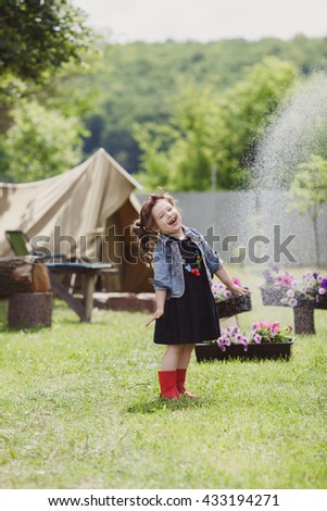 Pretty little girl dressed in a black dress denim jacket and red boots played in yard
