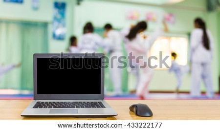 Computer on the table, blur image of taekwondo class as background.