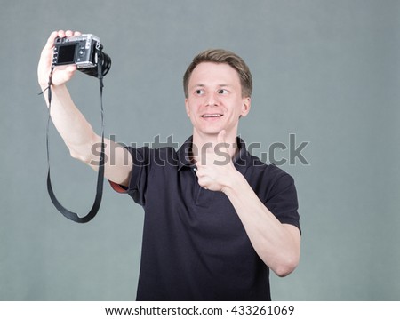 Young handsome guy taking selfie with retro style digital camera on grey background