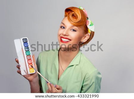 Creative artist. Close up portrait headshot red head beautiful young woman pretty smiling pinup girl green button shirt holding painting brushes looking at you camera with retro vintage 50's hairstyle