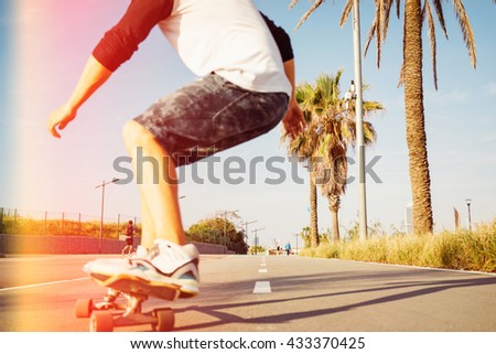 A man is skateboarding in a urban area with his back to the camera. Motion photo of a young guy on a longboard in a skatepark. Street photo with focus on landscape and flare light.
