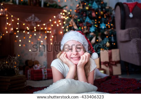 girl in Christmas cap lies on the background of fireplace and Christmas tree bright