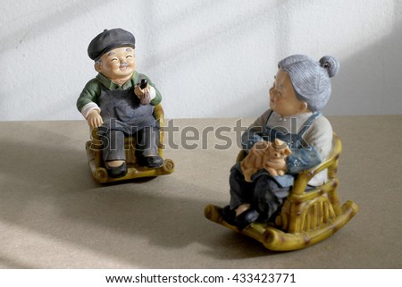 still life photography with lovely Grandpa is smoking and Grandma with cat doll siting rocking bamboo chair with low light from the window in the dark on wood background.