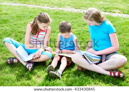 Friends children reading book outdoors on grass