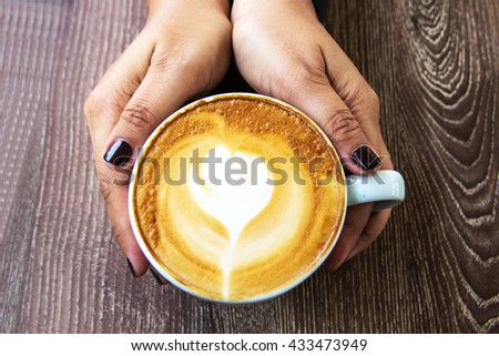 Woman holding hot cup of coffee and with heart shape