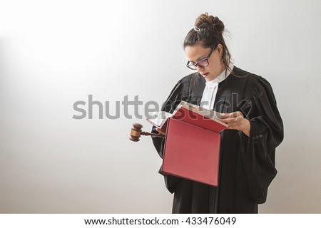thirty something brunette woman wearing a canadian lawyer toga with a gavel in her hands and reading a red criminal law book