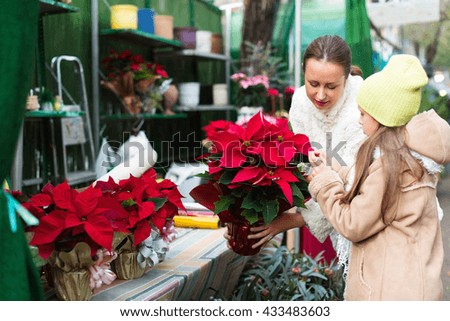 Mom with excited daughter buying Christmas star flower in market. Focus on woman