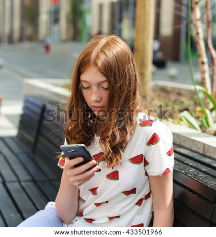 Girl texting on the smart phone and sitting in a bench in a city.
