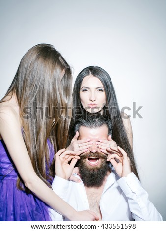Bearded handsome man screaming in white shirt with two young pretty women in violet dresses with long hair closing eyes in studio on grey background