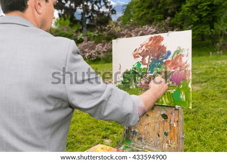 Male artist painting a standing in front of  a sketchbook during creation a beautiful sketch of picture outdoors