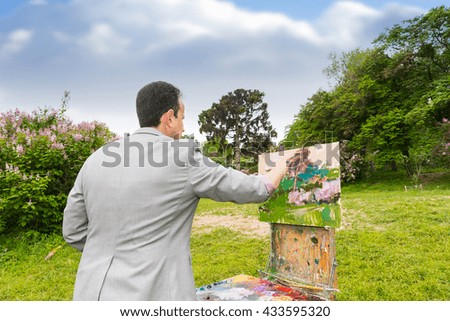 Middle-aged fashionable male professional artist working on a sketchbook painting a garden scene with flowers outdoors