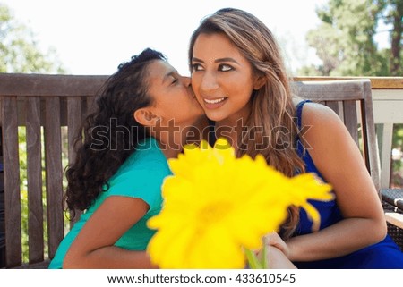 Girl kissing her mothers cheek on garden bench