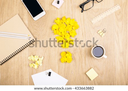 Top view of wooden desktop with crumpled yellow paper lightbulb, coffee, smartphone and various stationery items. Idea concept