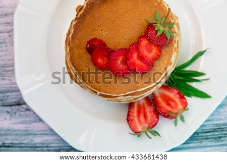 Pancakes with fresh strawberry and mint on white plate on blue wooden background. Top view.