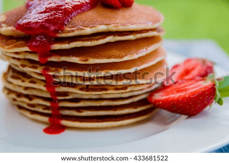 Pancakes with fresh strawberry and jam on white plate on white wooden background  in garden or on nature background.  Stack of pancakes on the table. Closeup.