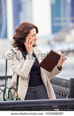Woman talking on cell phone and looking at the business notebook outdoors