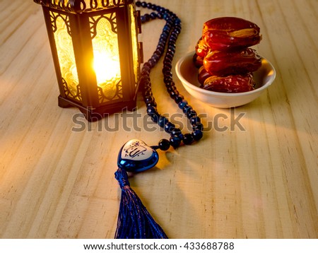 Allah, muslim God write in heart shape near dates fruits on white dish placed on wooden floor with shining lantern, dates are ready to serve in ramadan kareem night.