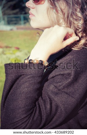 Blond curly model in black coat read bracelet on her wrist