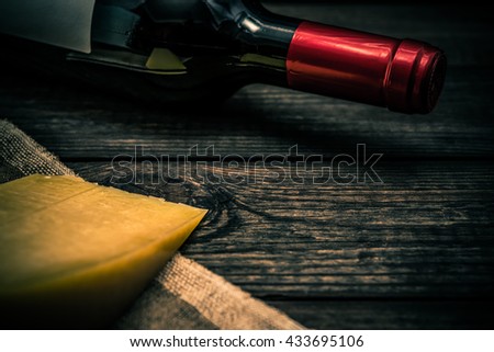 Bottle of red wine with a piece of parmesan lying on a piece of canvas on an old wooden table. Close up view, focus on the bottle of red wine, image vignetting and the orange-blue toning