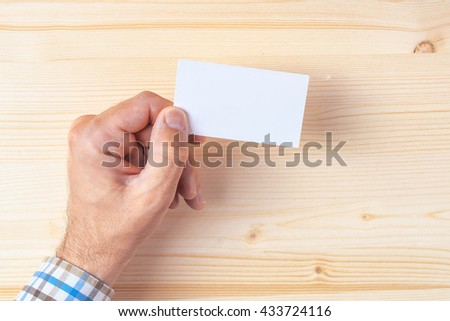 Top view of businessman holding blank business card on office desk, mock up copy space for graphic design or text placement.