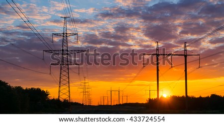 Silhouettes high voltage electric pylon in sunset background.