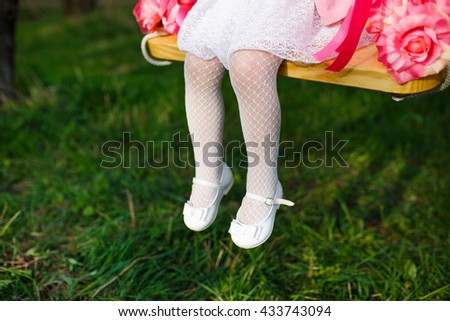 Little girl riding on a swing. legs close up on a background of green grass.