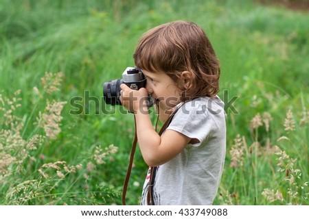 Little girl is photographing flowers in green grass by means of vintage camera.
