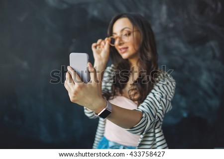 Young pretty woman with smartphone in her hand taking picture of herself in glasses