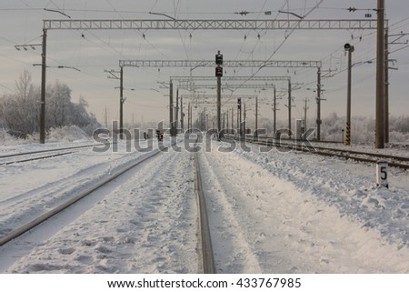 Electrified railway tracks with red railway signals - railway station with traffic sign in winter period
