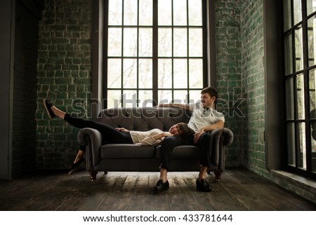 young couple sitting on a gray couch in front of a large loft windows Royalty-Free Stock Photo #433781644