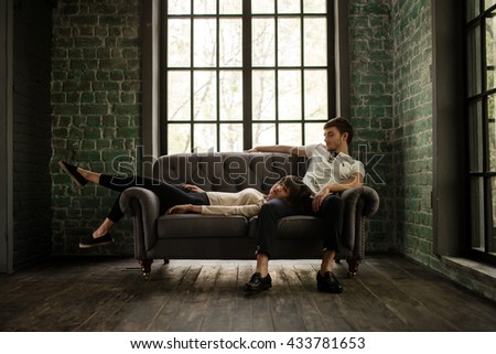 young couple sitting on a gray couch in front of a large loft windows Royalty-Free Stock Photo #433781653