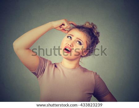 Closeup portrait young woman scratching head, thinking deeply about something, looking up, isolated on gray wall background. Human facial expression, emotion, feeling, sign body language