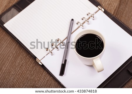 Coffee cup with notebook on wood background.
