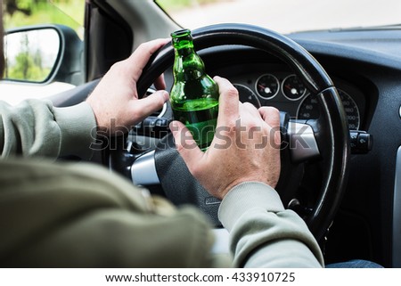 In the picture a man drinking alcohol in the car.