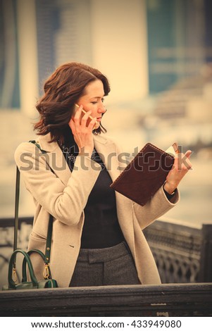 Woman talking on cell phone and looking at the business notebook outdoors. instagram image filter retro style