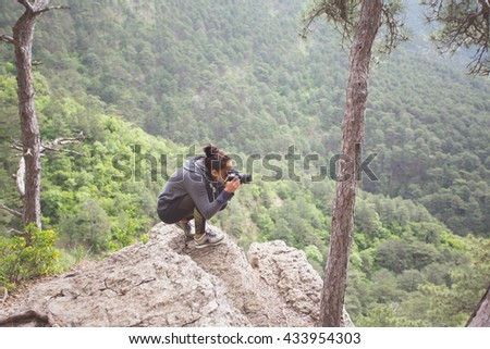 Adventurous female photographer sitting on the rock while photographing mountains.