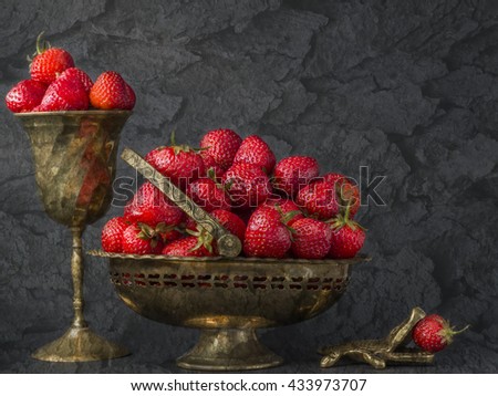 Still life with strawberries.Closeup of strawberry fruits with an iron  vase and goblet with alligator on dark background.Red berry strawberry