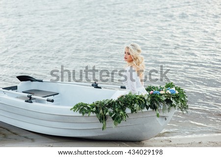 Beautiful young bride woman in luxury wedding dress with red lips makeup and long wavy hairstyle. Beauty girl portrait posing in the boat, outdoor photo.