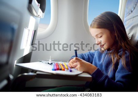 Adorable little girl traveling by an airplane. Child sitting by aircraft window and drawing a picture with colorful pencils.