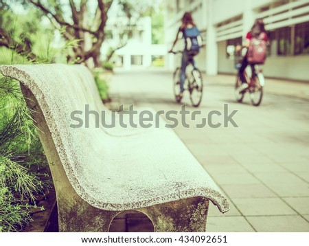 Vintage style photo of sitting bench with blurred bicycling students in the campus