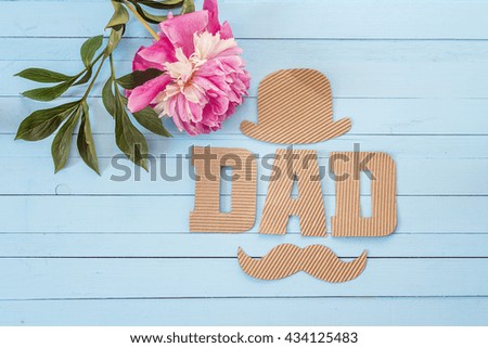 Cardboard letters, hat, mustache and peony on blue painted boards. Father's Day background
