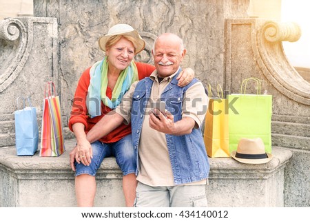 Senior couple taking selfie after shopping with smartphone - Happy tourist in the 60's having fun with new technologies outdoor - Travel lifestyle concept with retired people - Warm filter