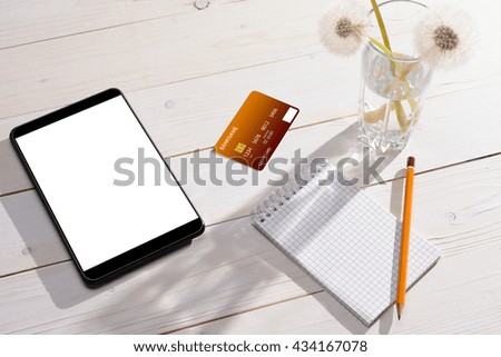 Credit card, tablet and notebook with a pencil on a white wooden table