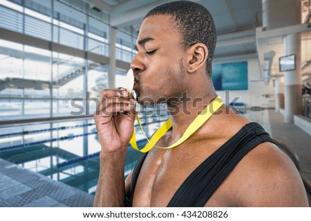 Happy athlete kissing medal against empty swimming pool with large windows