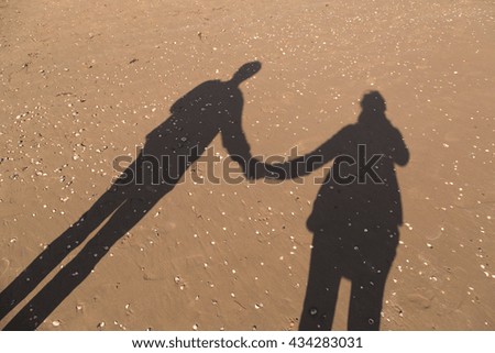 Shadows of couple in love on a walk. Man and woman holding hands on walk on sandy beach with shells. 
