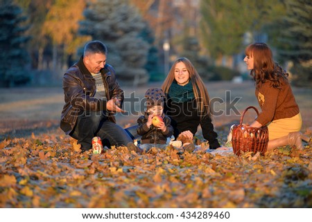 Happy family resting in a park in autumn. Family sitting in the yellow autumn leaves. Cheerful family relaxing in the park in autumn. Kid eating an apple in the park in autumn.